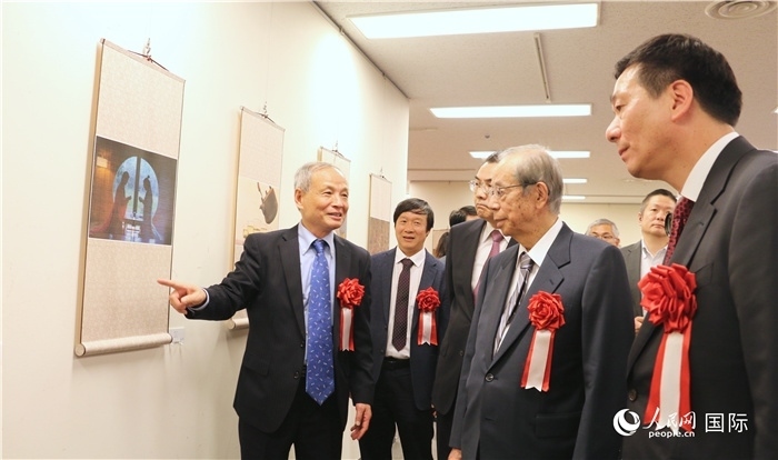 “湖州印象”攝影展主創(chuàng)、世界華人攝影協(xié)會(huì)副會(huì)長馮學(xué)敏向吳江浩大使、福田康夫前首相等嘉賓介紹展出作品。（人民網(wǎng) 許可攝）