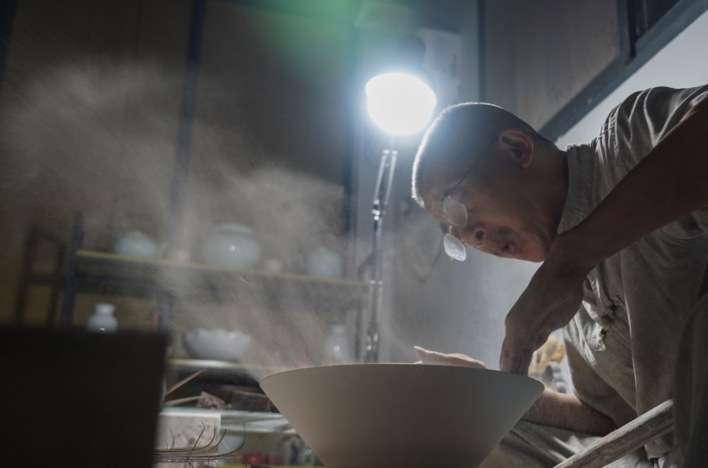 ↑ 在景德鎮(zhèn)，手工匠人吹去坯內(nèi)的泥土（2021年7月14日攝）。