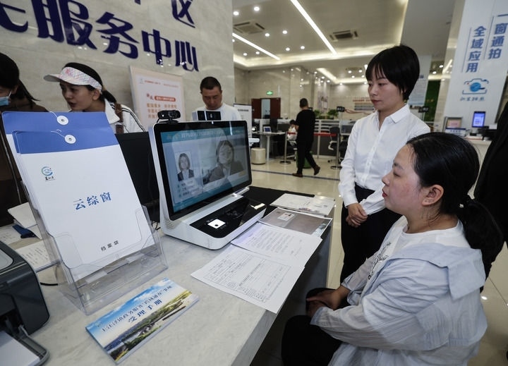 在浙江省嘉興市秀洲區(qū)王江涇鎮(zhèn)便民服務(wù)中心的“跨域通辦·云綜窗”窗口，辦理開業(yè)登記的個體工商戶（右一）通過該系統(tǒng)與江蘇省蘇州市吳江區(qū)盛澤鎮(zhèn)行政審批局工作人員視頻連線，進行身份讀取及材料線上審核（2024年5月9日攝）。新華社記者 徐昱 攝