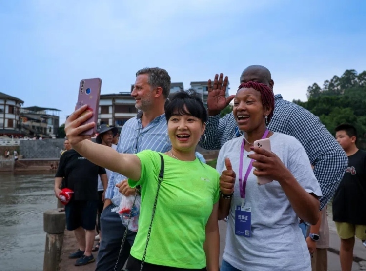 2024“一帶一路”媒體合作論壇聯(lián)合采訪調(diào)研行成員在樂(lè)山蘇稽古鎮(zhèn)與游客合影留念。本報(bào)記者 伊霄攝