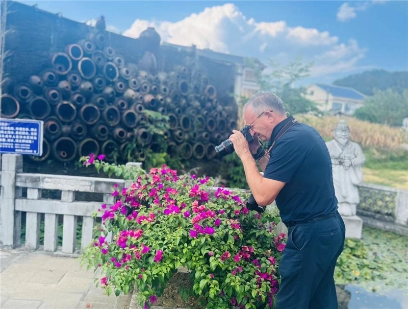 遠處黔北民居錯落有致，近處一只黑色的蝴蝶穿梭于粉紫色三角梅花叢間隙，與俄羅斯“大歐亞”總編輯弗拉基米爾·別列日內(nèi)赫的鏡頭玩起了捉迷藏，“你追我逃，不亦樂乎”。（張亞欣攝）