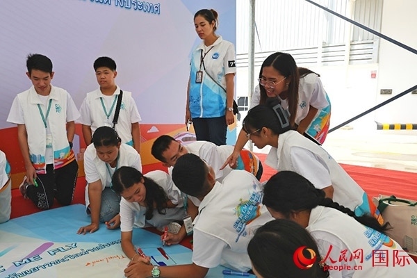 泰國學(xué)生在開營儀式展板上繪制圖案。人民網(wǎng)記者 白元琪攝